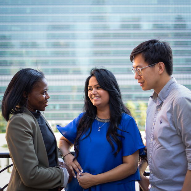 Three UNFCU staff members having a conversation in front of the United Nations building.