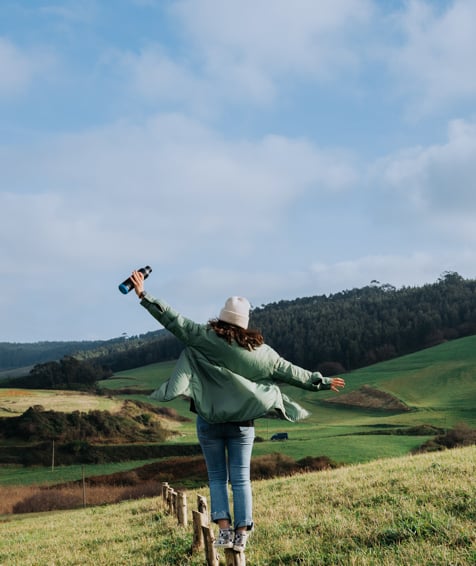 Individual on a hillside holding a metal water bottle.