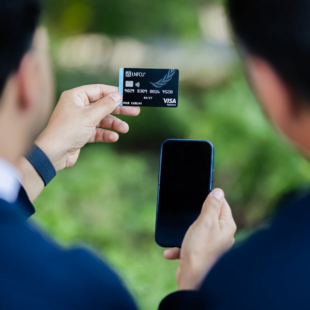 Two individuals looking at UNFCU Elite credit card and cellphone.