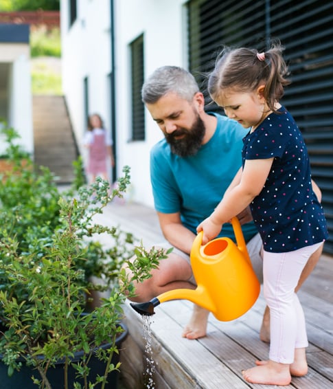 Individual and their child watering a plant.