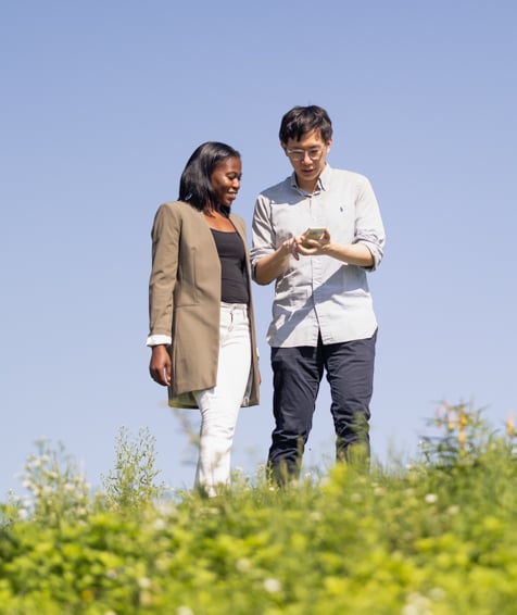 Two individuals looking at a cellphone while walking outdoors.