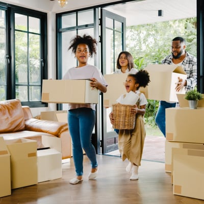 Two individuals and their children moving boxes into their new home.