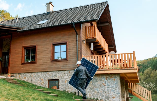 Individual carrying a solar panel next to a house.