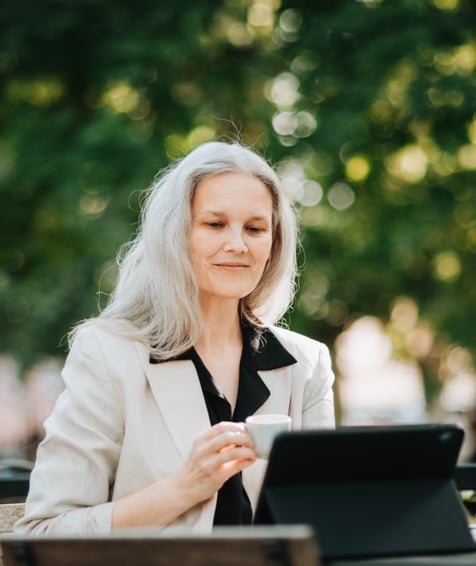 Individual looking at tablet and holding a coffee.